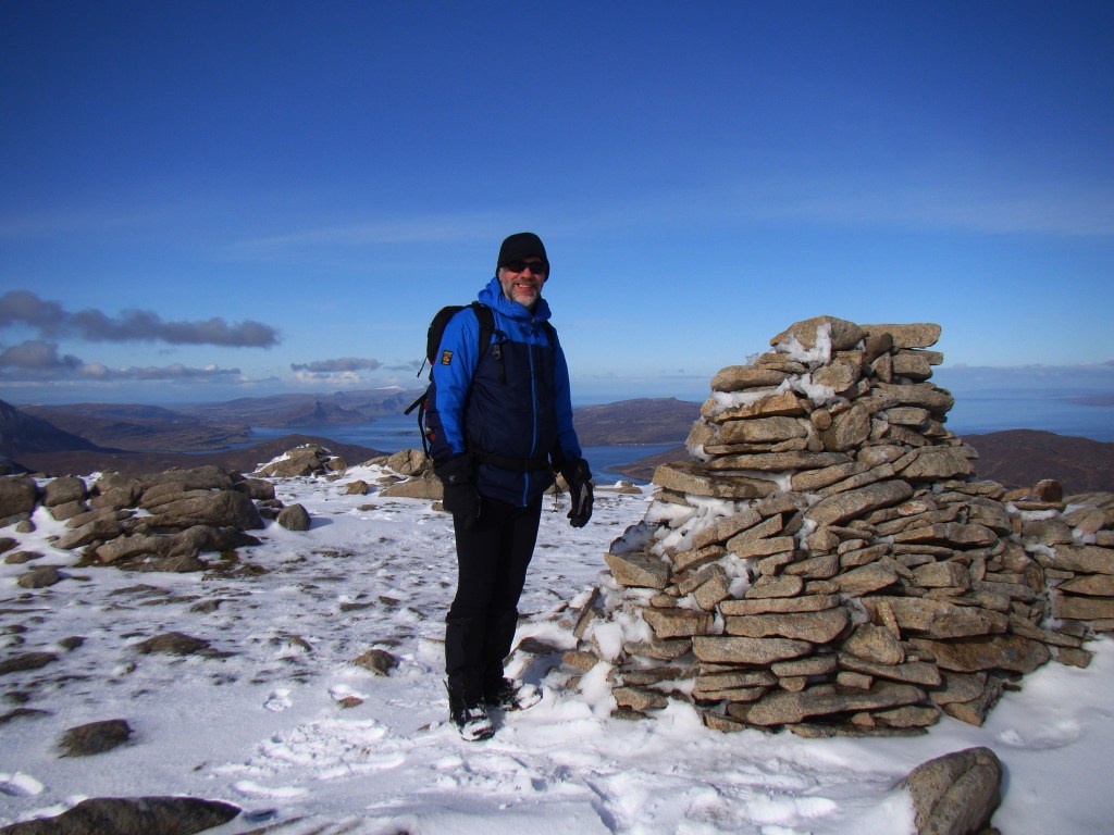 Nic on a snowy mountain beside a cairn